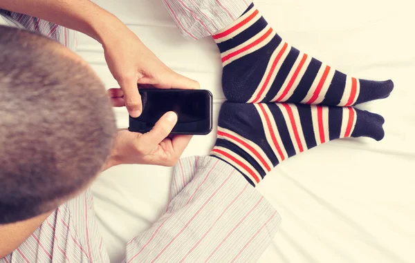 Joven usando un teléfono inteligente en la cama — Foto de Stock