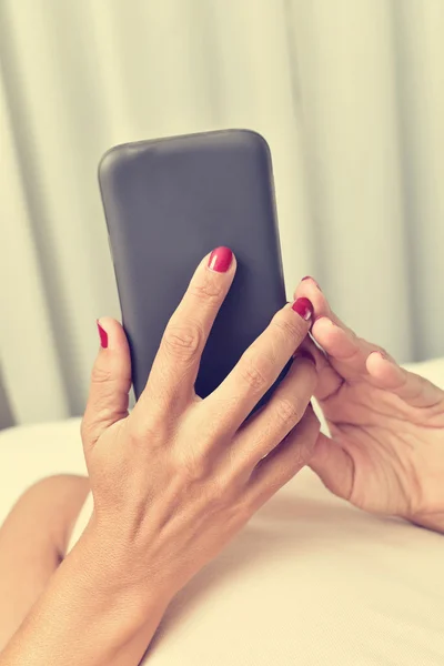 Jovem mulher usando um smartphone na cama — Fotografia de Stock