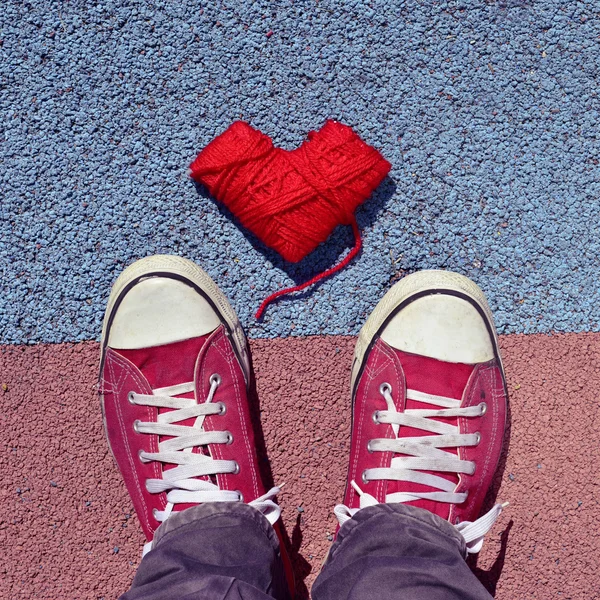 Hombre en zapatillas y bobina en forma de corazón de hilo en el asfalto — Foto de Stock