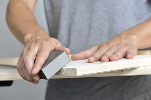 Man sanding a wooden board with a sanding block — Stock Photo, Image