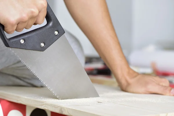 Joven aserrando una tabla de madera con una sierra de mano — Foto de Stock