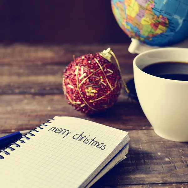 Bauble, xícara de café, globo e texto Feliz Natal — Fotografia de Stock