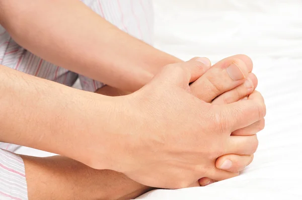 Young man in pajamas grabbing his feet with his hands — Stock Photo, Image