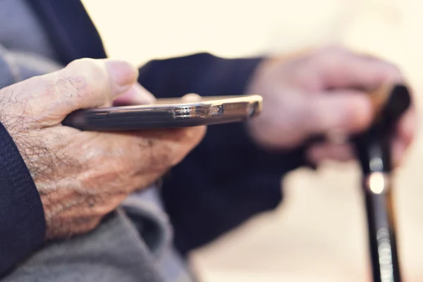 Old man with a walking stick uses a smartphone — Stock Photo, Image