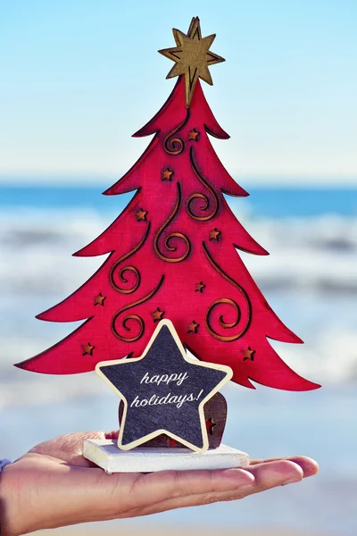 Árbol de Navidad y texto felices fiestas en la playa —  Fotos de Stock