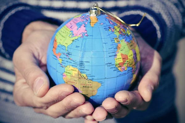 Hombre joven con un mundo globo como una bola de Navidad en sus manos — Foto de Stock