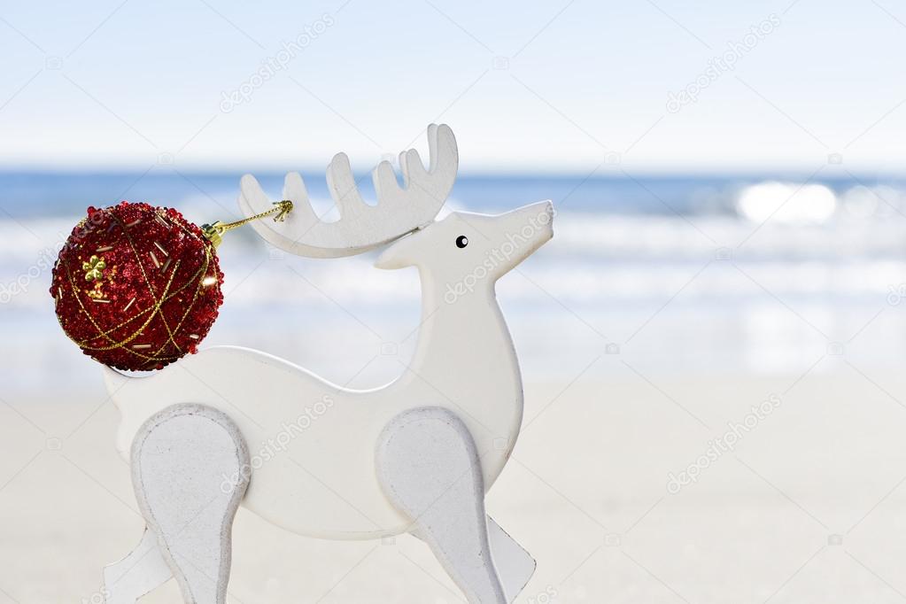 christmas ball in the antler of a wooden reindeer on the beach