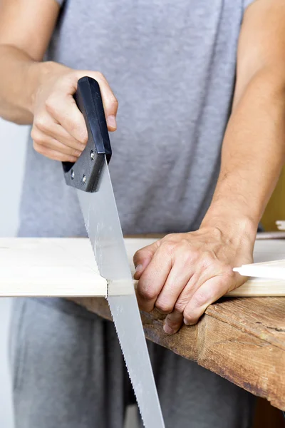 Young man sawing a wooden board with a handsaw — Stock Photo, Image