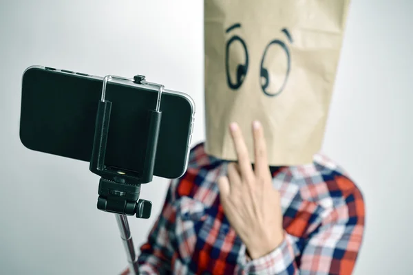 Jeune homme avec un sac en papier dans la tête prenant un selfie — Photo