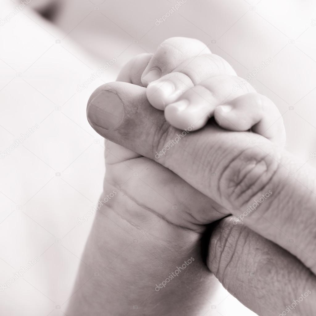 baby gripping the finger of an adult, in black and white