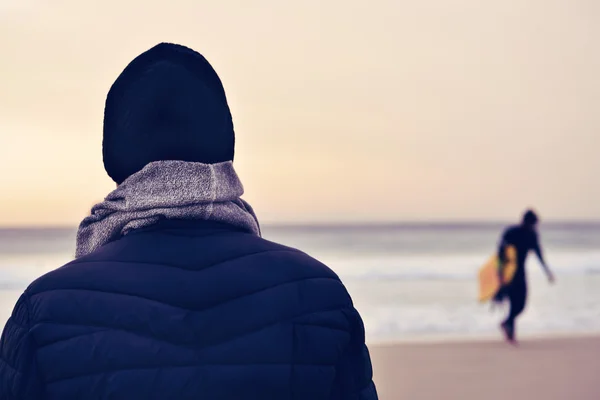 Uomo che indossa cappotto, sciarpa e berretto a maglia di fronte all'oceano — Foto Stock