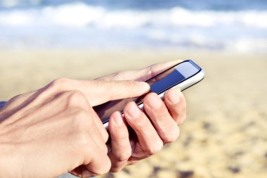 denizin yanında bir akıllı telefon kullanan genç adam