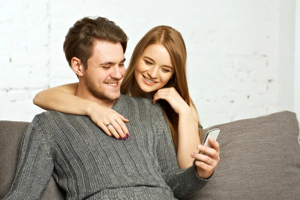 Pareja sentada en el sofá, viendo algo en el teléfono móvil — Foto de Stock