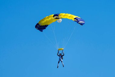 Mavi gökyüzüne karşı sarı ve mavi paraşütlü paraşütçü