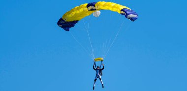Mavi gökyüzüne karşı sarı ve mavi paraşütlü paraşütçü