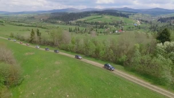 Geländewagen-Konvoi unterwegs durch die Berge der Karpaten. die Kamera fliegt über Bäume und Felder über Felsen und Wiesen — Stockvideo