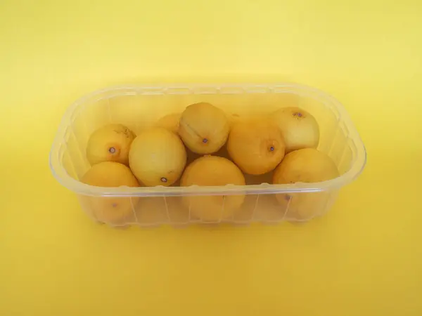 黄色の背景にプラスチック製の箱にレモン果実 Citrus Limon が入っています — ストック写真