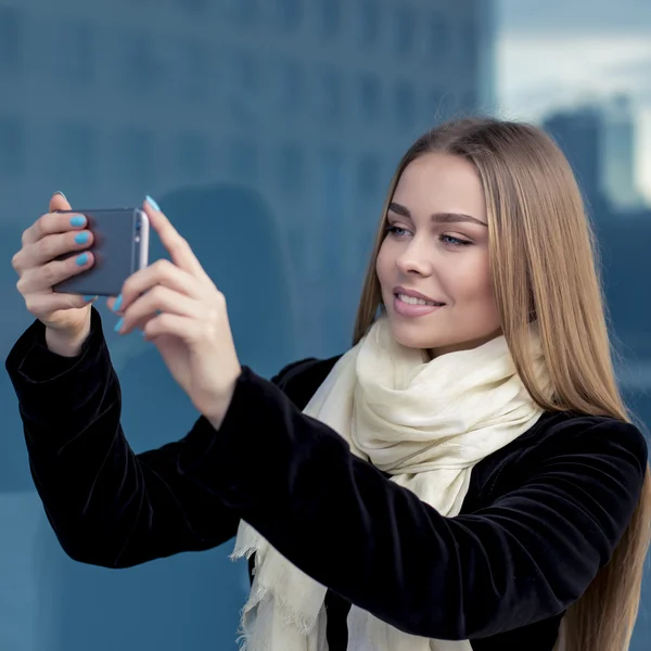 Очаровательная молодая женщина крупным планом в черном читает сообщение на мобильный телефон, против синего — стоковое фото