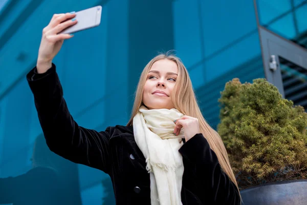 Молодая смешная женщина делает селфи на смартфоне против синего — стоковое фото
