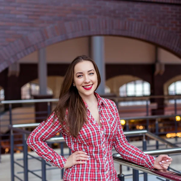 Jonge mooie krullend vrouw in plaid shirt en spijkerbroek die zich voordeed en glimlachen — Stockfoto