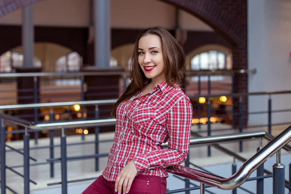 Jovem mulher bonita encaracolado em camisa xadrez e jeans posando e sorrindo — Fotografia de Stock