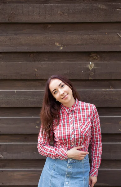 Atraktivní brunetka v červené kostkované košili na pozadí dřevěné stěny — Stock fotografie