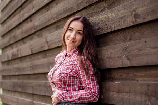 Młoda brunetka w plaid shirt stojący na tle drewniany dom — Zdjęcie stockowe