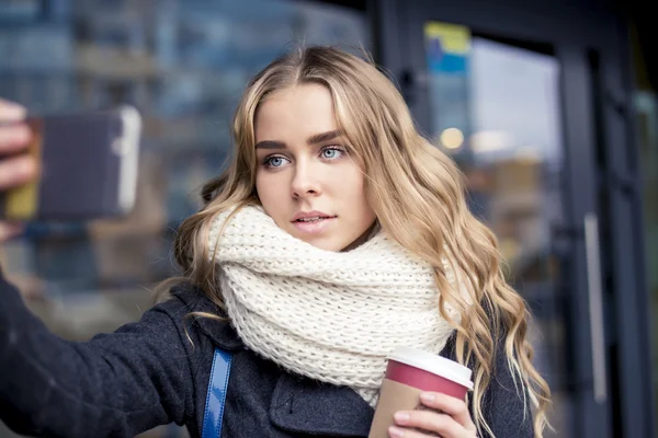 Jonge en mooie vrouw met behulp van de telefoon houden van een kopje koffie in het donkere café — Stockfoto