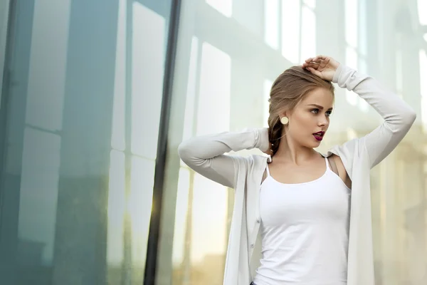 Blonde met donkerrood lippenstift in de buurt van het glas van een modern gebouw — Stockfoto