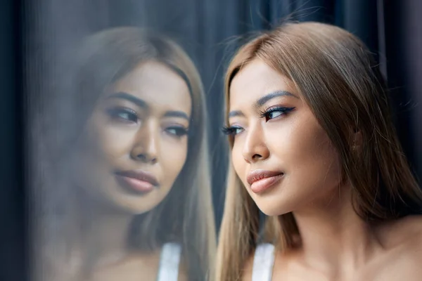 Outdoor close-up fashion portrait of young beautiful Asian woman posing near to window