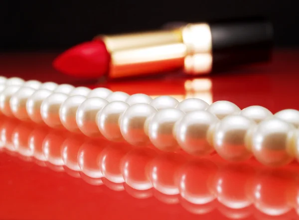 Perlas y lápiz labial sobre rojo — Foto de Stock