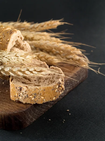 Bread on wooden board with wheat — Stock Photo, Image