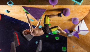 Genç adam tırmanma salonunda kaya tırmanışı yapıyor, zorlu problemleri çözmeye çalışıyor.