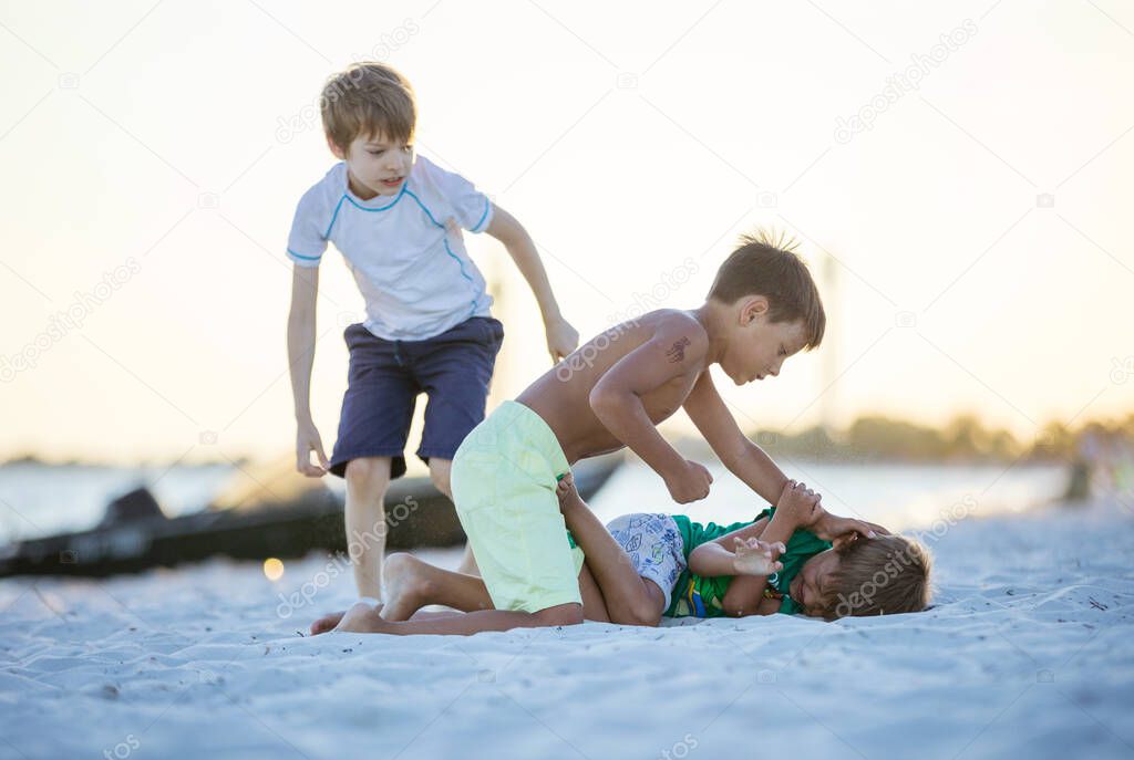 Young boys fighting on beach, older boy going to hit younger one. Siblings rivalry.