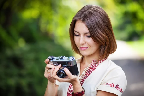 Oung woman looking at screen of retro style camera and smiling — Stock Photo, Image