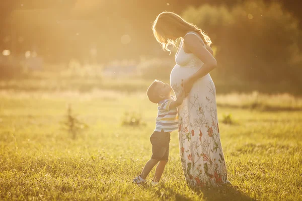 Liten pojke kysser magen av hans gravid mamma utomhus — Stockfoto