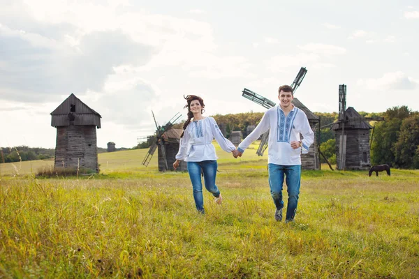 Joyeux jeune couple courant sur le terrain, contre quelques vieux moulins en arrière-plan — Photo