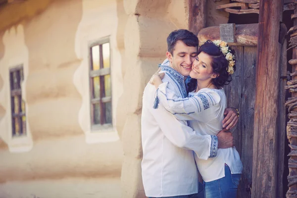Young couple in Ukrainian style clothes standing at the entrance of rural house — Stock Photo, Image