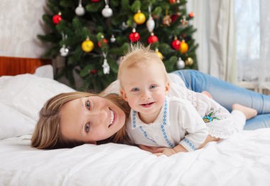 Mutlu anne ve bebek çocuk evde yatakta portre ile süslenmiş Noel ağacı arka planda