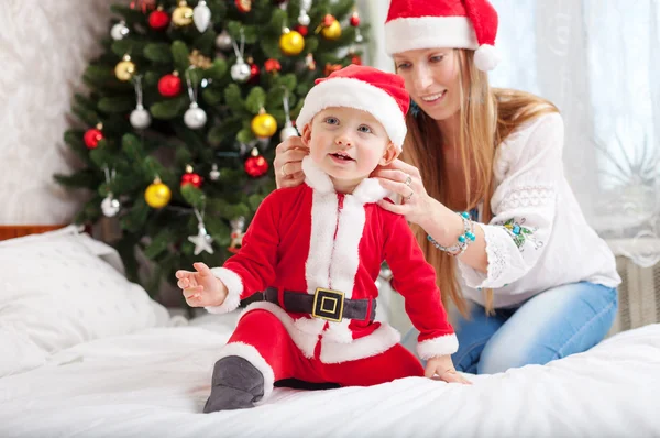 Feliz madre poniendo traje de Papá Noel en su hijo pequeño en casa —  Fotos de Stock