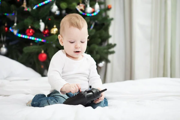 Småbarn pojke anläggning Rc controller medan du sitter på sängen hemma i juletid — Stockfoto