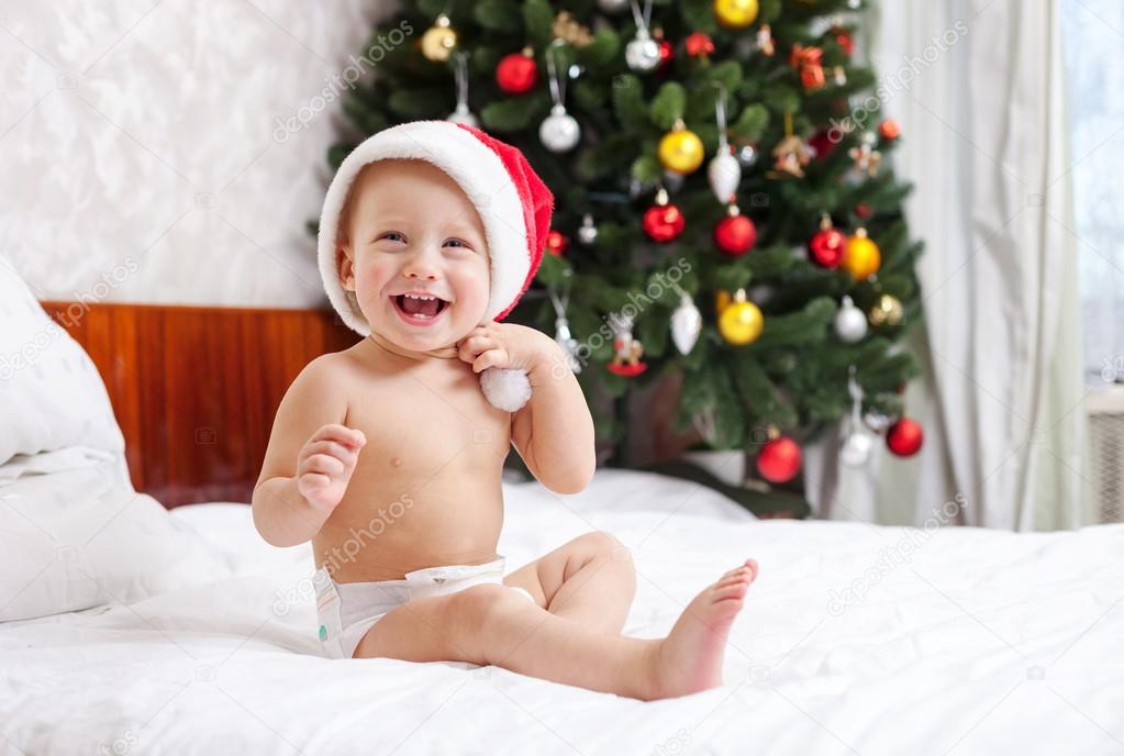 Christmas baby in santa hat sitting on bed and laughing