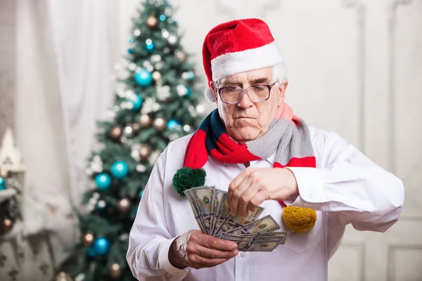 Senior man in Santa's hat holding money over Christmas background — Stock Photo, Image