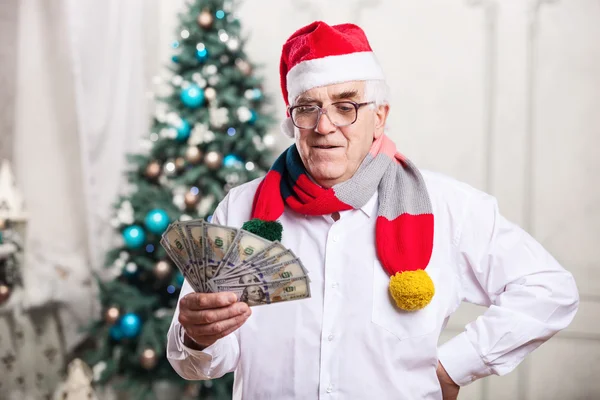 Senior man in Santa's hat holding money against Christmas background — Stock Photo, Image