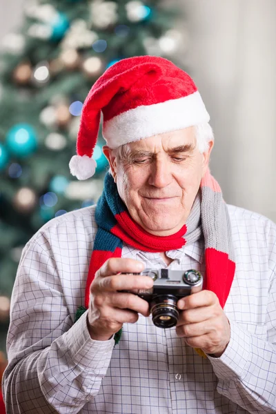 Senior man looking at display of retro style camera and smiling against Christmas background — Stock Photo, Image