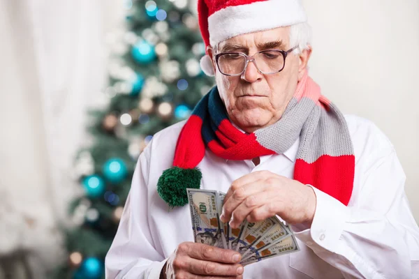 Senior man in Santa's hat holding money over Christmas background — Stock Photo, Image