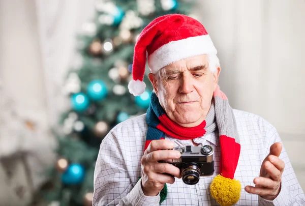 Senior man in Santa hat looking at display of retro style camera — Stock Photo, Image