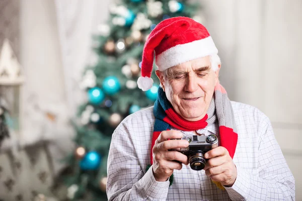 Senior man looking at display of retro style camera and smiling against Christmas background — Stock Photo, Image