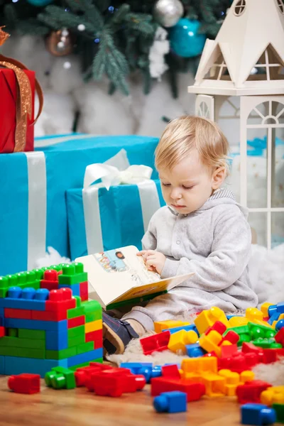 可爱的蹒跚学步的儿子竟然坐在圣诞树和看书 — 图库照片