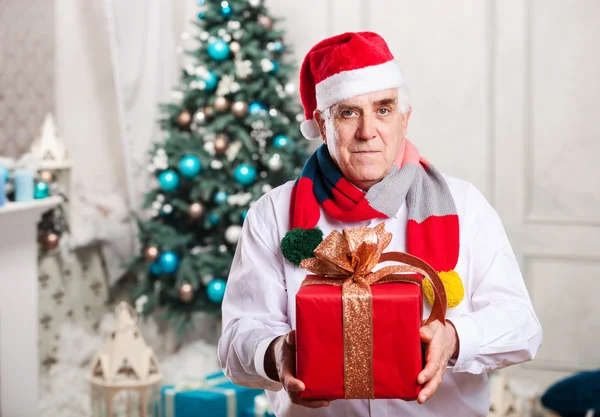 Senior man holding a red gift box on Christmas background — Stock Photo, Image